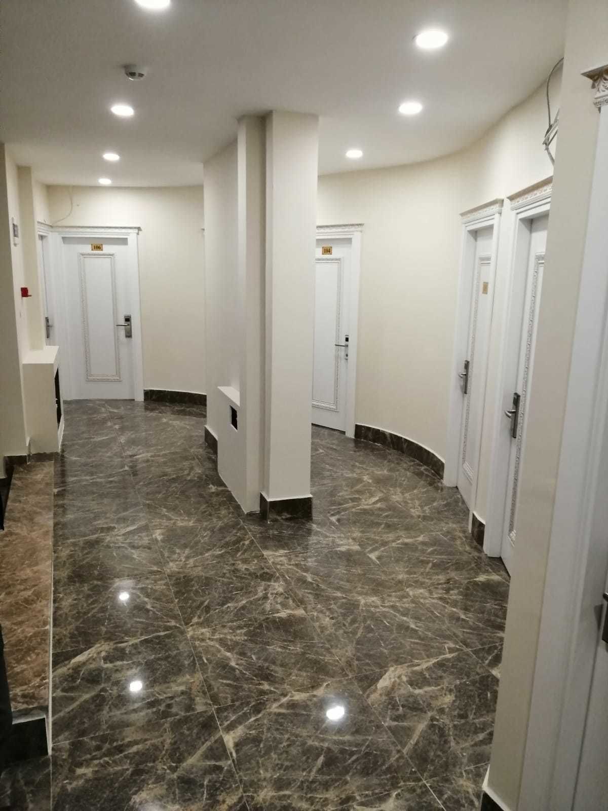 Un pasillo con suelo de mármol, paredes blancas y puertas numeradas que señalan la ubicación de las habitaciones.