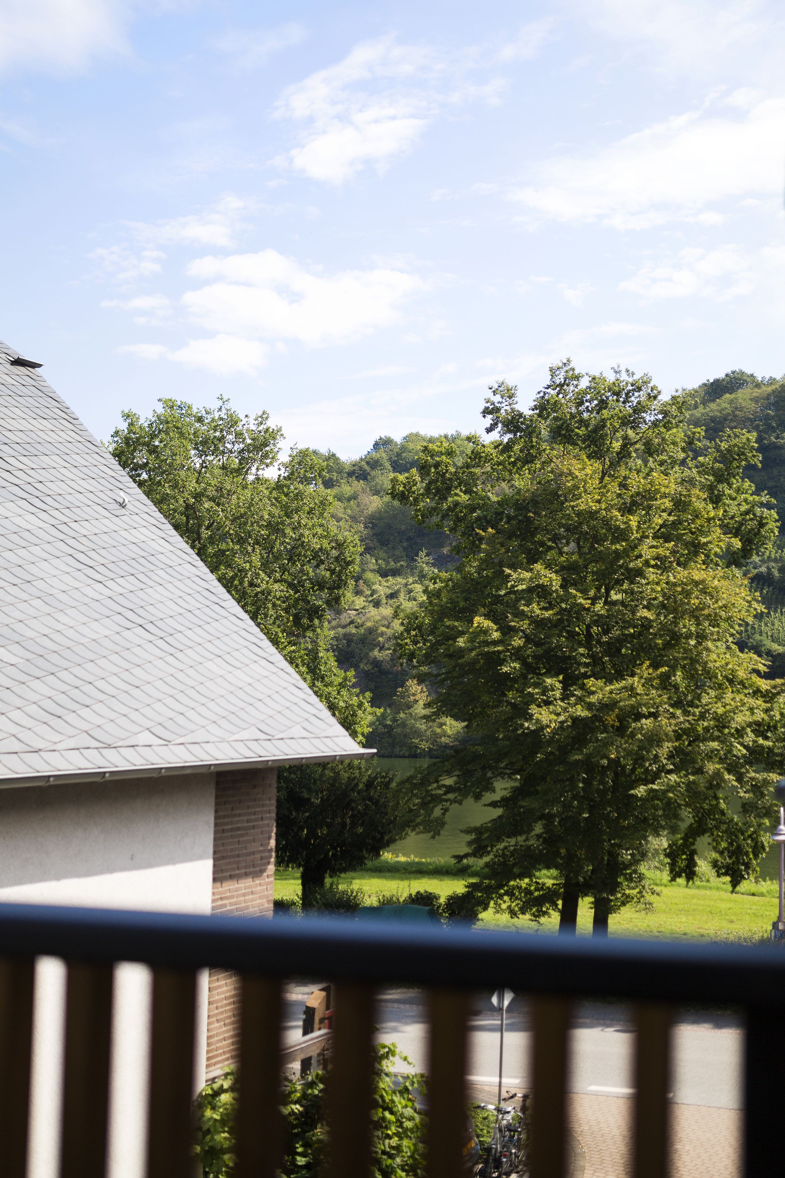 A view from a balcony with a brick building, a tree-lined hill, and a clear sky.