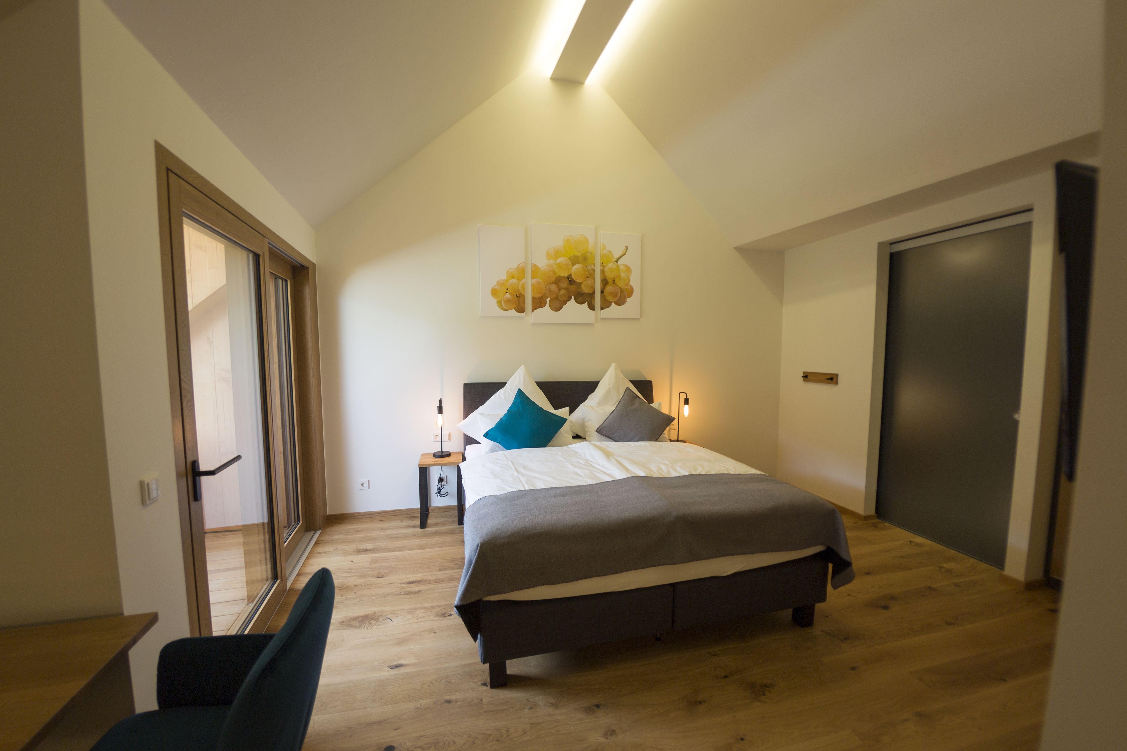 A bedroom with a bed, a chair, a bedside table, a lamp, and a door.