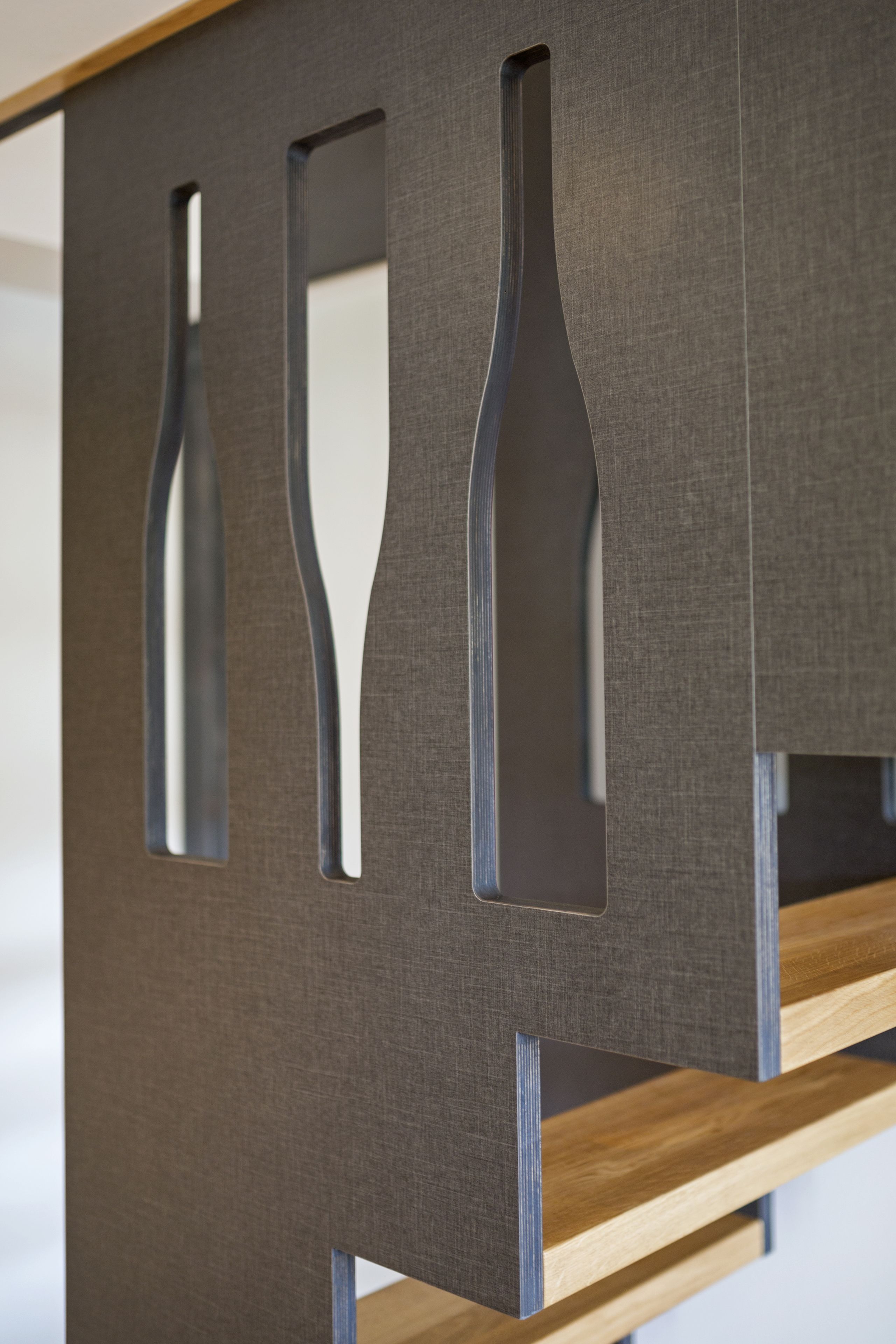 A modern room with a wooden floor, a grey textured wall, and a metal partition with cut-out shapes.