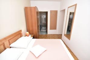 A hotel room with a bed, a wooden wardrobe, a mirror, and a bathroom visible through an open door. - Rooms Tom (Malinska-Dubasnica)