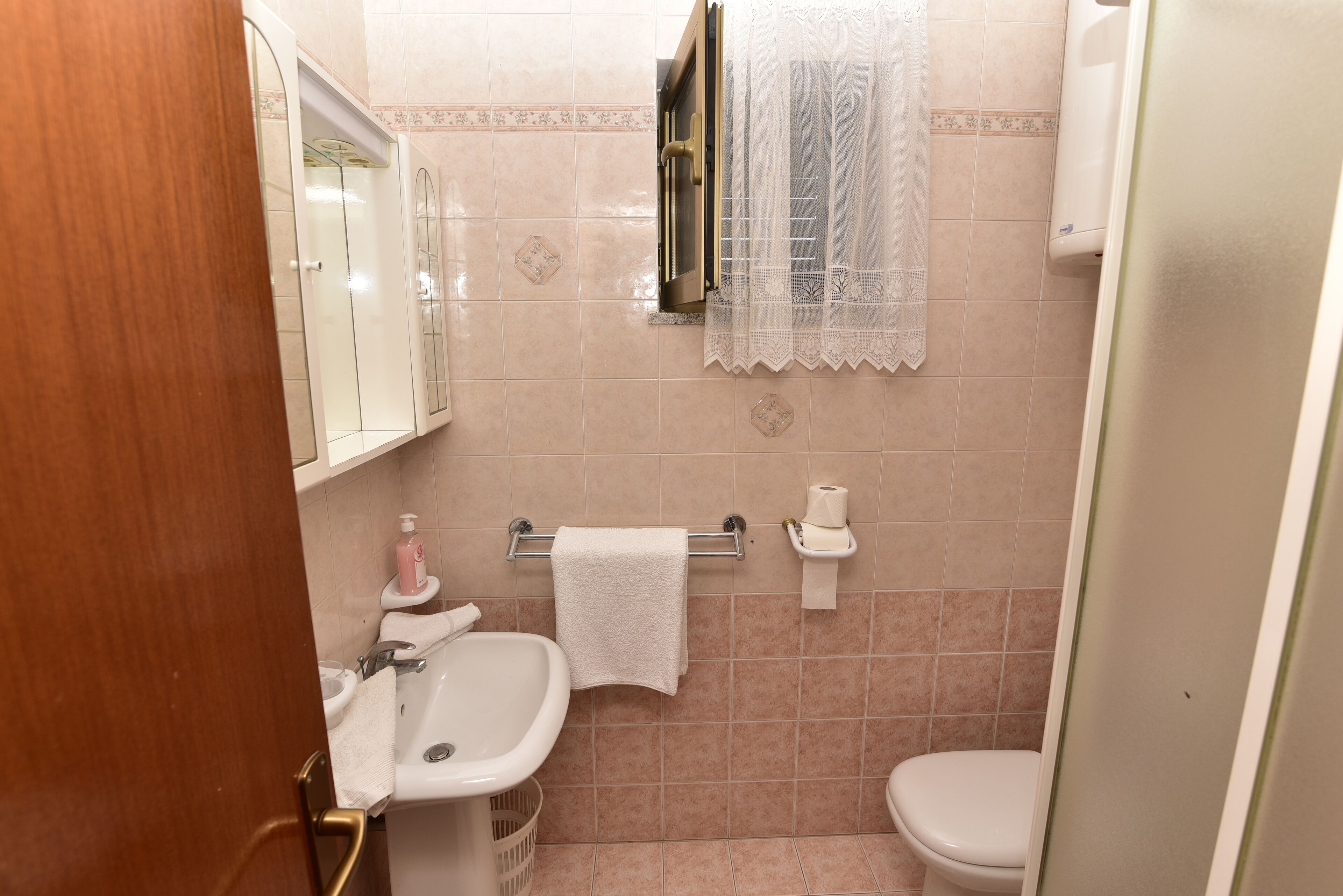 Une salle de bain avec un lavabo, des toilettes et une fenêtre avec un rideau.