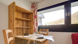 Una mesa de madera con sillas, una ventana con cortinas y vistas al exterior.
