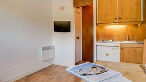 Un espacio habitable compacto con kitchenette, televisor montado y comedor con mesa y sillas.