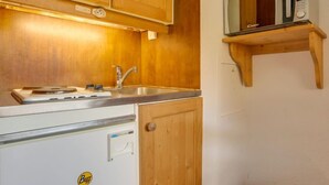 Cocina compacta con armarios de madera, un estante para microondas integrado y un lavamanos.