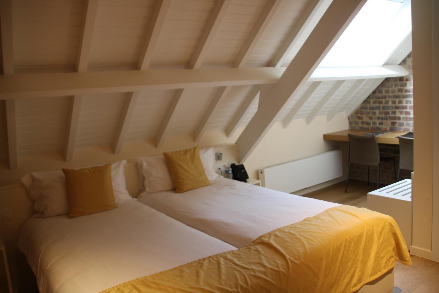 A bedroom with a loft-style ceiling, a bed with white and yellow bedding, a desk, and a chair.