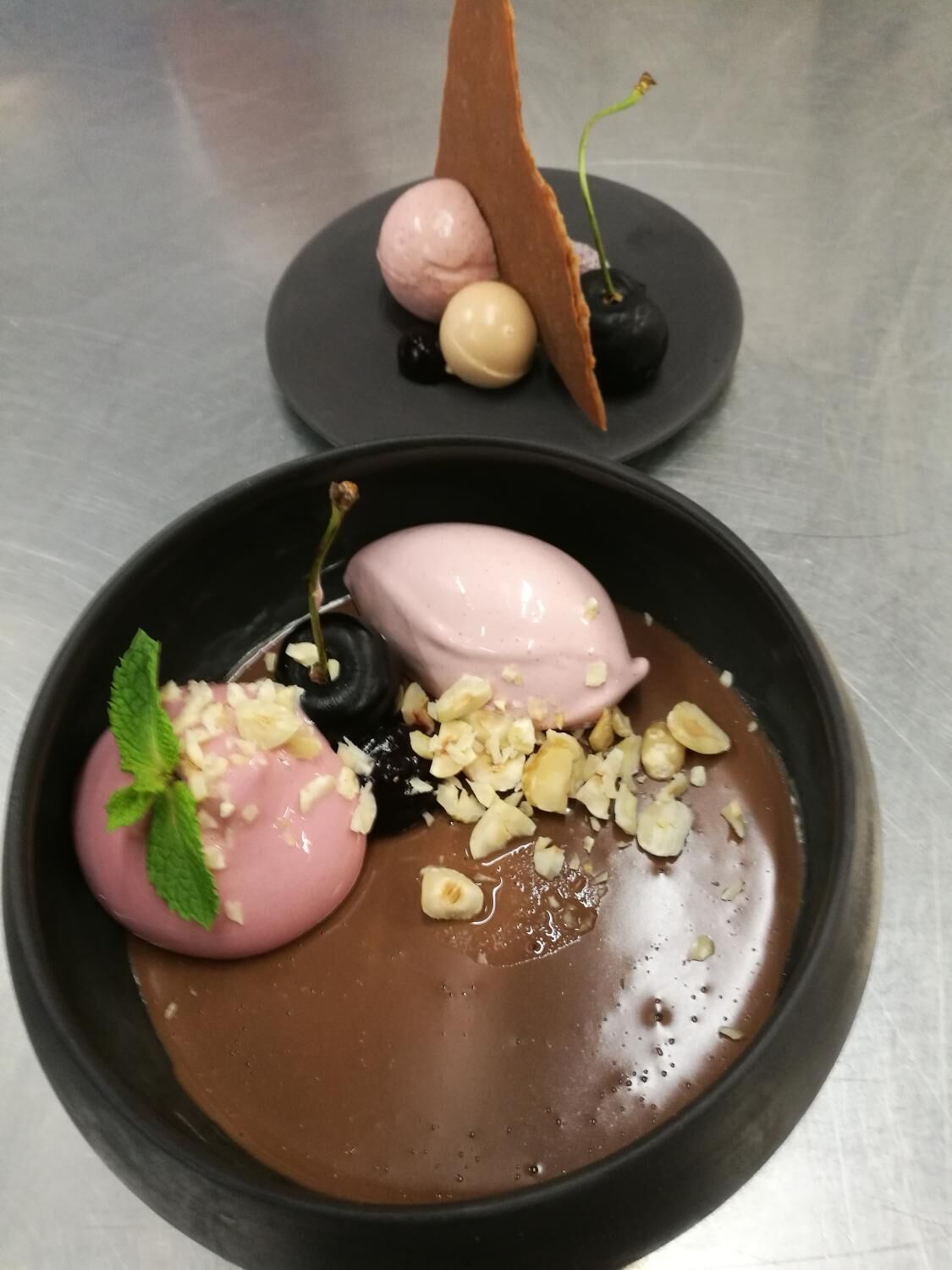 A dessert with chocolate sauce, a pink dessert, and a chocolate-covered cherry on a plate.