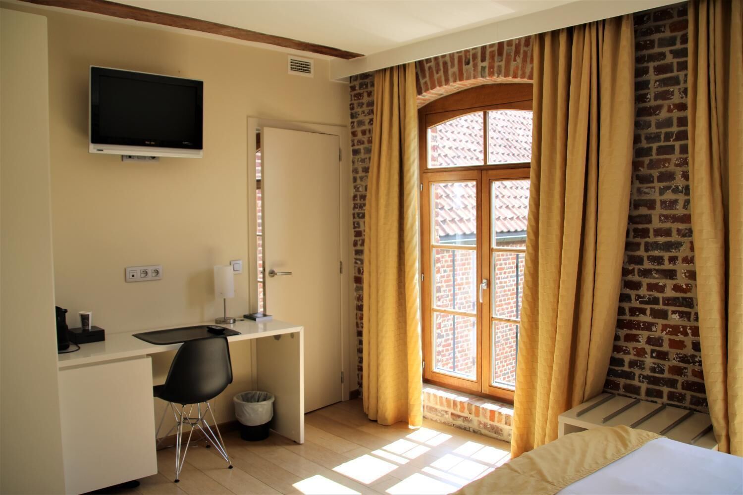A hotel room with a desk, chair, TV, and a window with curtains.