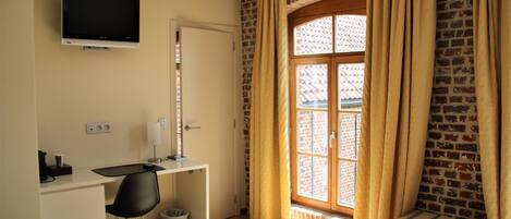A hotel room with a desk, chair, TV, and a window with curtains.