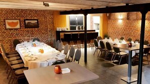 A conference room with long tables and chairs, a brick wall, and a kitchen area in the background. - Hostellerie de Biek (Aalst)