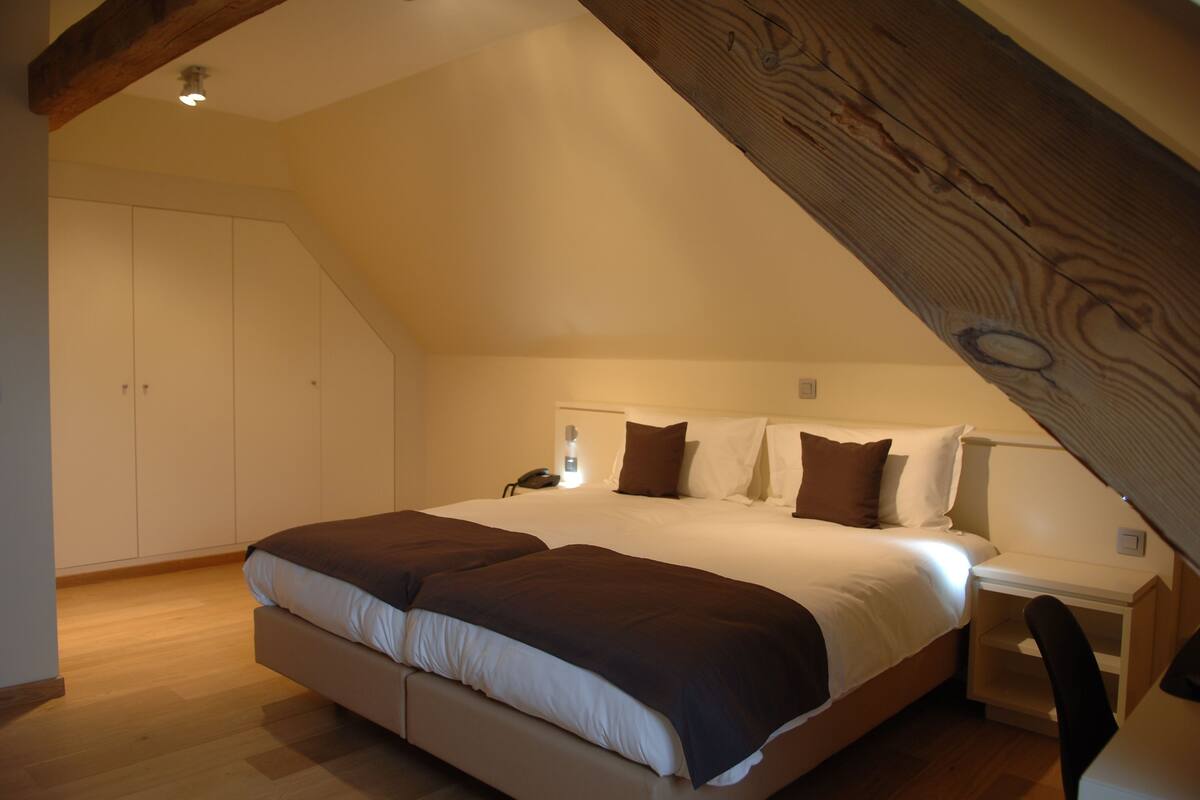 Un dormitorio con una cama grande, vigas de madera, un escritorio y un armario.