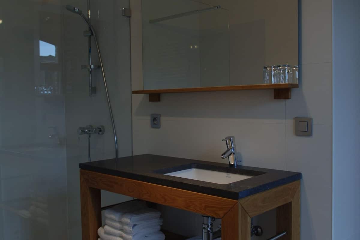 Un baño con cabina de ducha de vidrio, tocador de madera con lavamanos y espejo sobre el tocador.