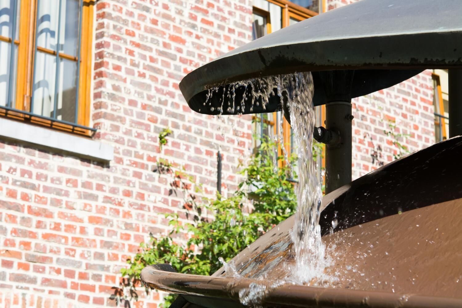 Un élément décoratif aquatique avec un bec en métal et un mur de briques en arrière-plan.