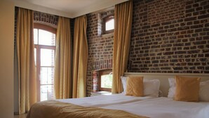 A hotel room with a large bed, beige curtains, and a brick wall. - Hostellerie de Biek (Aalst)