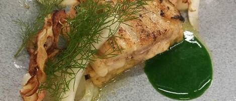 A plate of food with a piece of grilled fish, garnished with dill and crispy elements, served on a speckled ceramic plate.