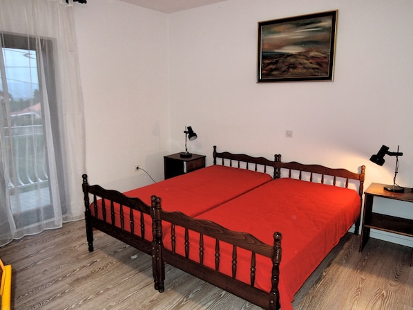 A bedroom with a wooden bed, a red bedspread, a nightstand with a lamp, and a painting on the wall.