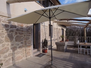 Relax in the shaded patio area, surrounded by lush greenery and a wooden pergola.