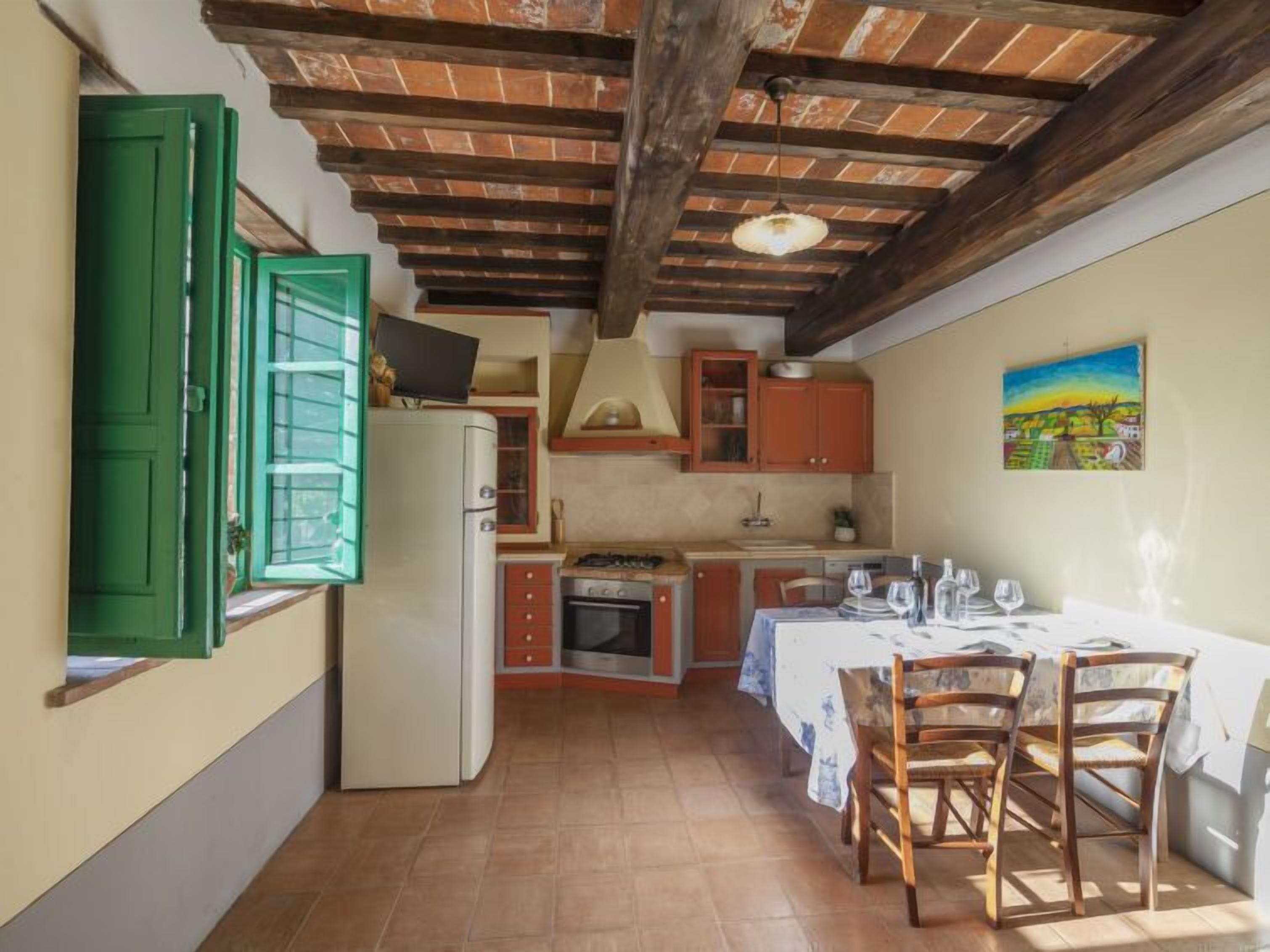 Una cucina compatta con zona pranzo, caratterizzata da travi a vista in legno, un frigorifero e un tavolo apparecchiato.
