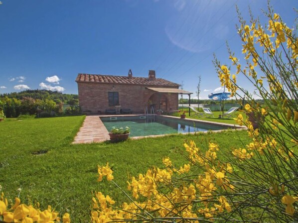 A brick house with a swimming pool, surrounded by a grassy lawn and yellow flowers.