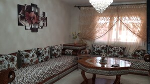 A living room with a patterned sofa, a coffee table, and a chandelier. - Lilia-appart (Oujda)