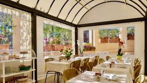Un espace repas avec des tables dressées pour le service, un chariot de service et des plantes en pot.