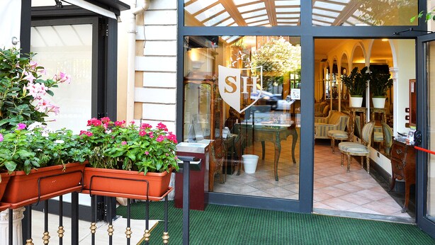 L’entrée d’un hôtel, avec une porte en verre, une enseigne et un espace détente comprenant des chaises et des tables à l’intérieur.