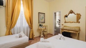 Une chambre d’hôtel avec deux lits, une coiffeuse avec un miroir, une petite table avec des articles de toilette et un tableau au mur.
