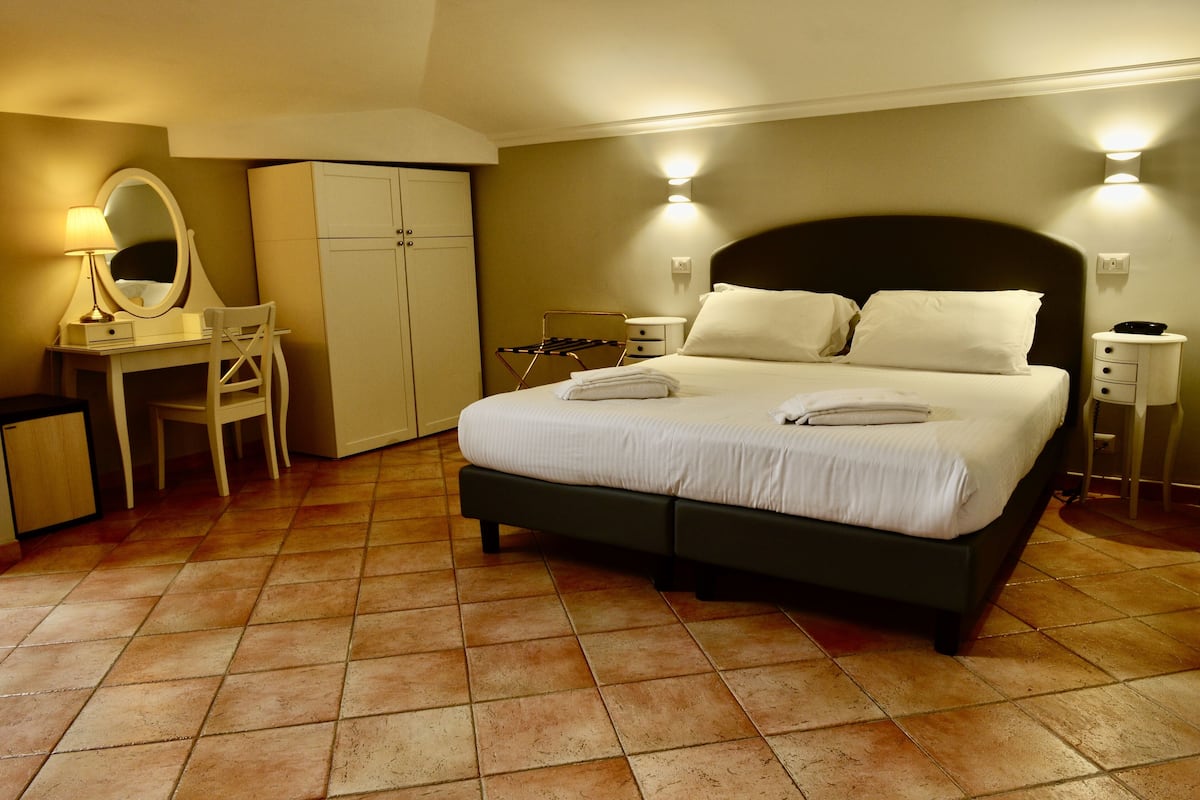 A bedroom with a bed, a desk with a mirror, a wardrobe, and a nightstand.
