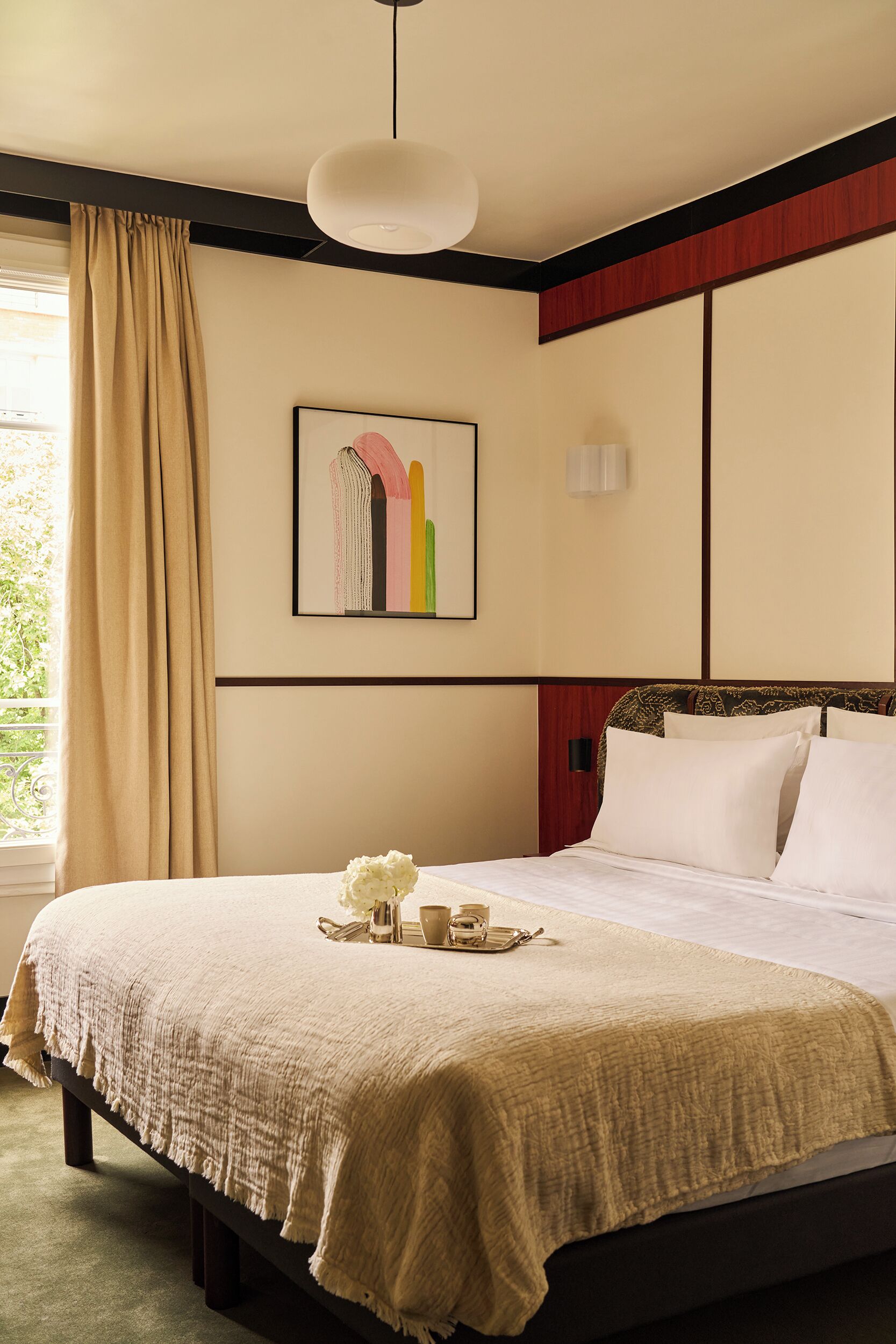 A neatly made bed with a beige blanket, a bedside table with a white flower, and a framed artwork on the wall.