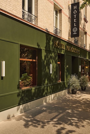 A hotel facade with a green exterior, large windows, and a sign reading 'HOTEL MARGUERITE.'