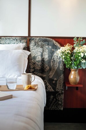 A bed with a patterned headboard, a bedside table with a vase of flowers, and a tray with a glass of water and a mug. - Hôtel Marguerite (Paris)