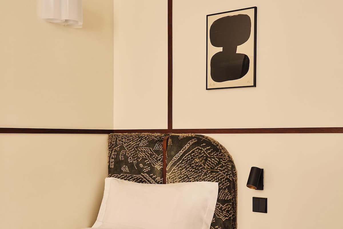 A neatly made bed with a white sheet, a dark headboard, a bedside table with a lamp, and a framed picture on the wall.