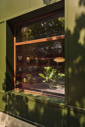 Una ventana con vista a una habitación que contiene estanterías, una planta en maceta y un lámpara colgante.