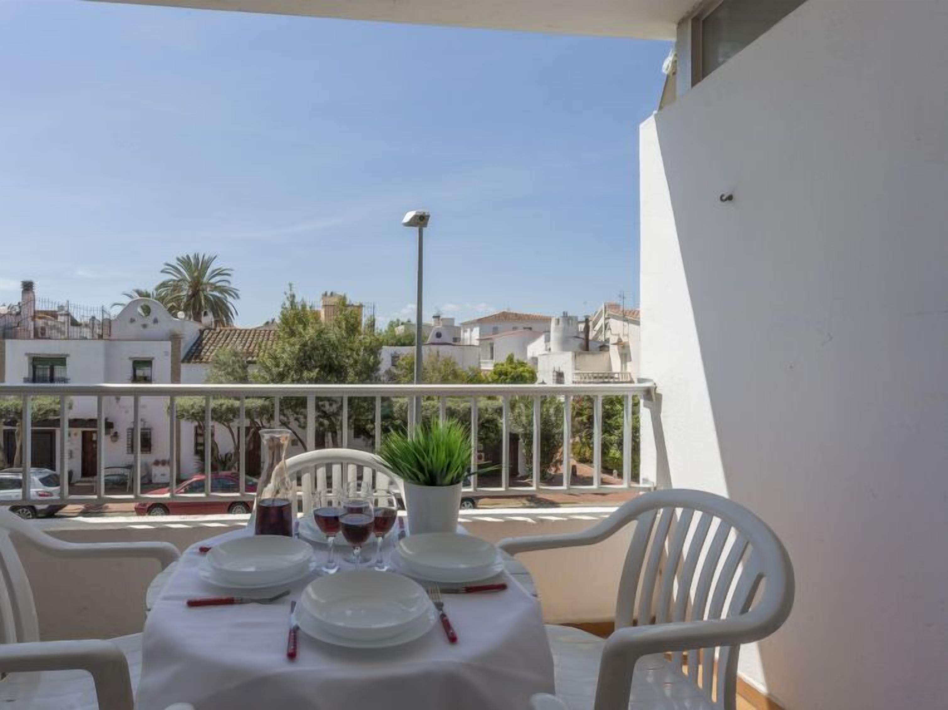 Un balcon avec une table dressée pour le repas, des chaises blanches et une plante en pot.