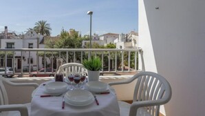 Un balcon avec une table dressée pour le repas, des chaises blanches et une plante en pot.