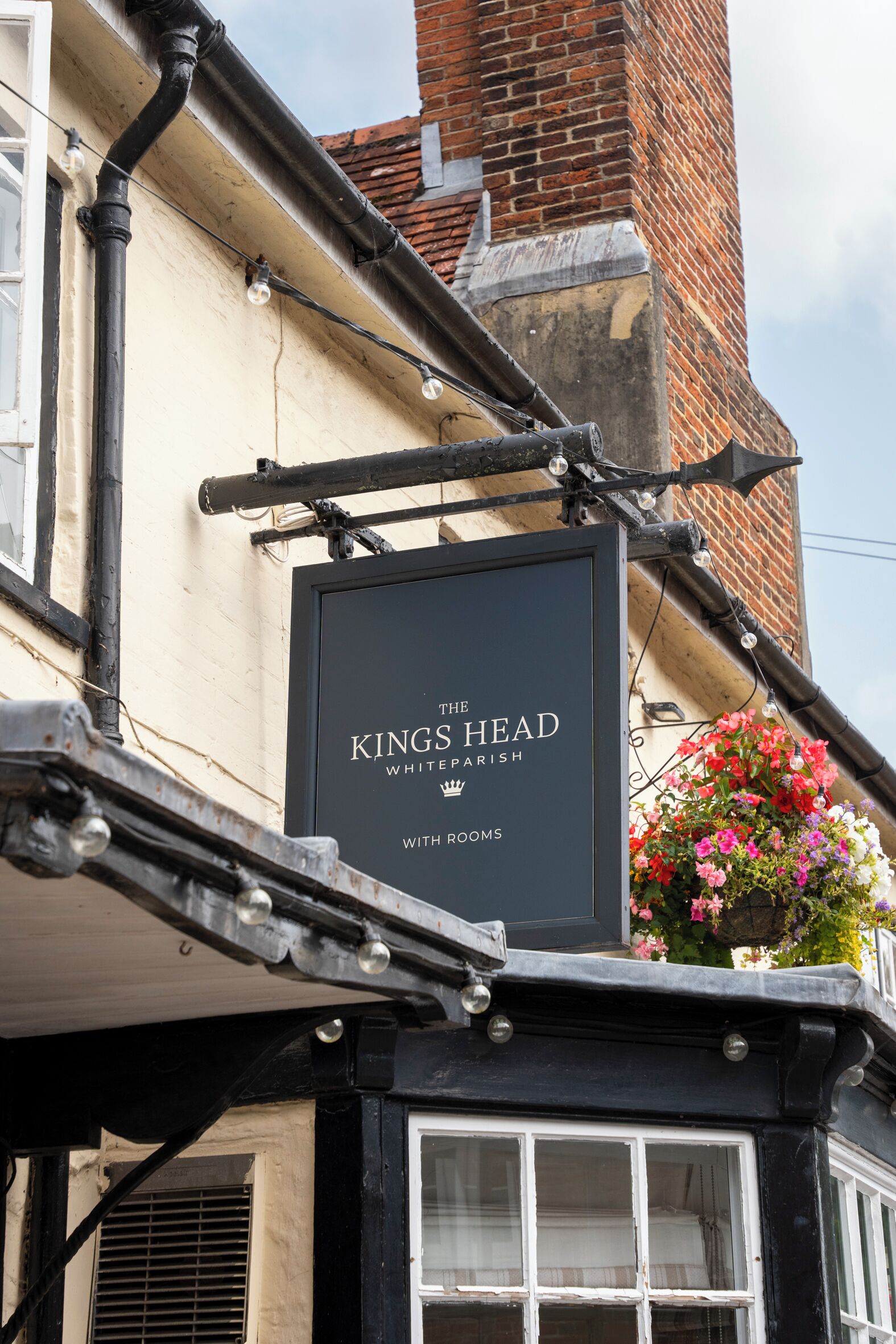 Un letrero negro con el texto "The Kings Head White Parish" y "With Rooms", que indica un pub con habitaciones.