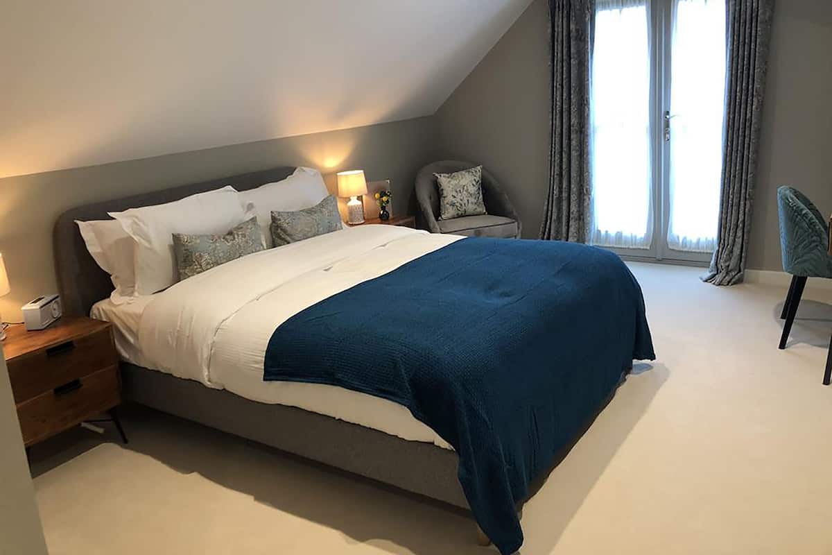 A modern bedroom with a large bed, bedside tables, a chair, and a window with curtains.