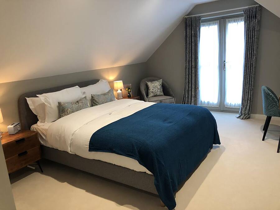 Un dormitorio moderno con una cama grande, mesitas de noche, una silla y un ventanal con cortinas.