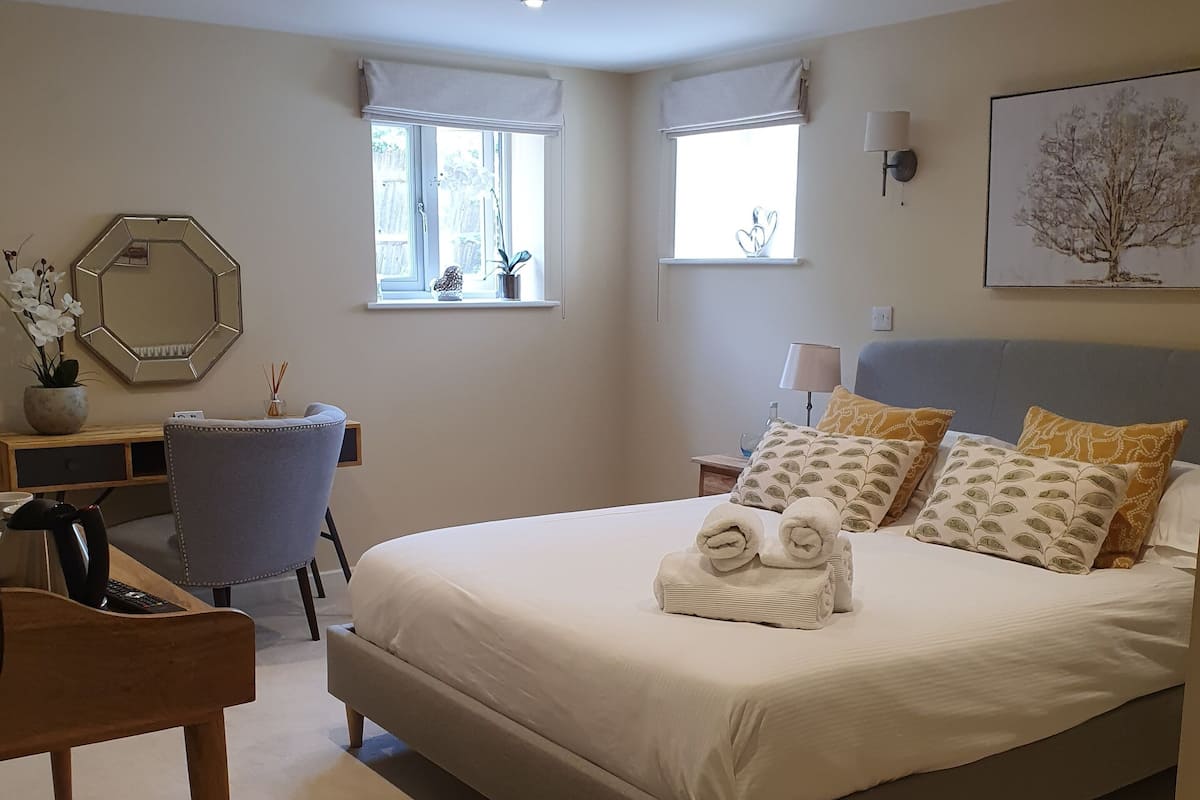 A bedroom with a large bed, two bedside tables, a chair, a desk, and a window.