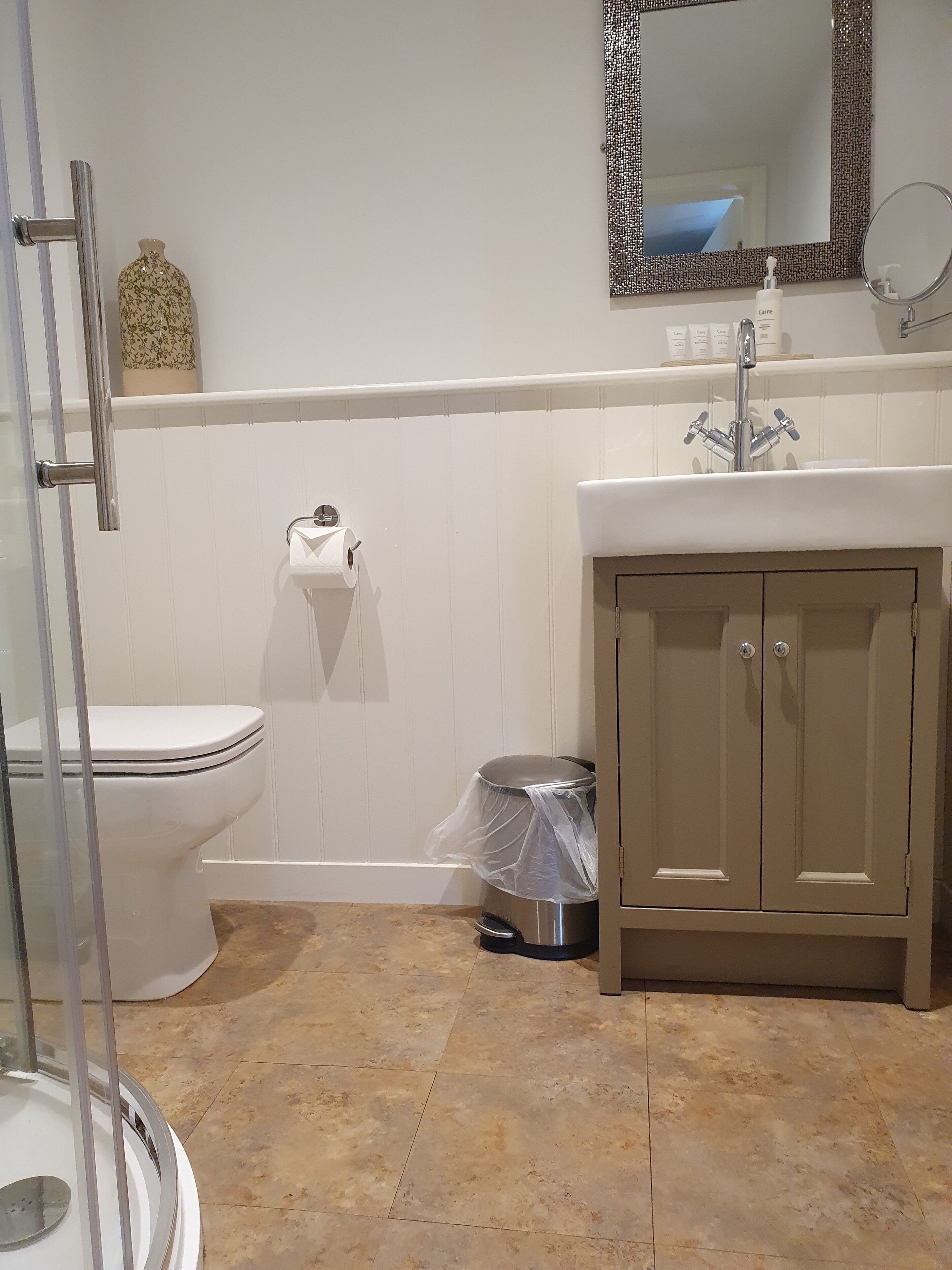 Un baño con inodoro, lavamanos, espejo y cubo de basura.