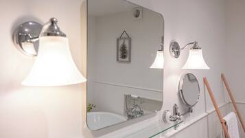 A bathroom with a large mirror, two wall-mounted lights, a glass shelf, and a towel rack.