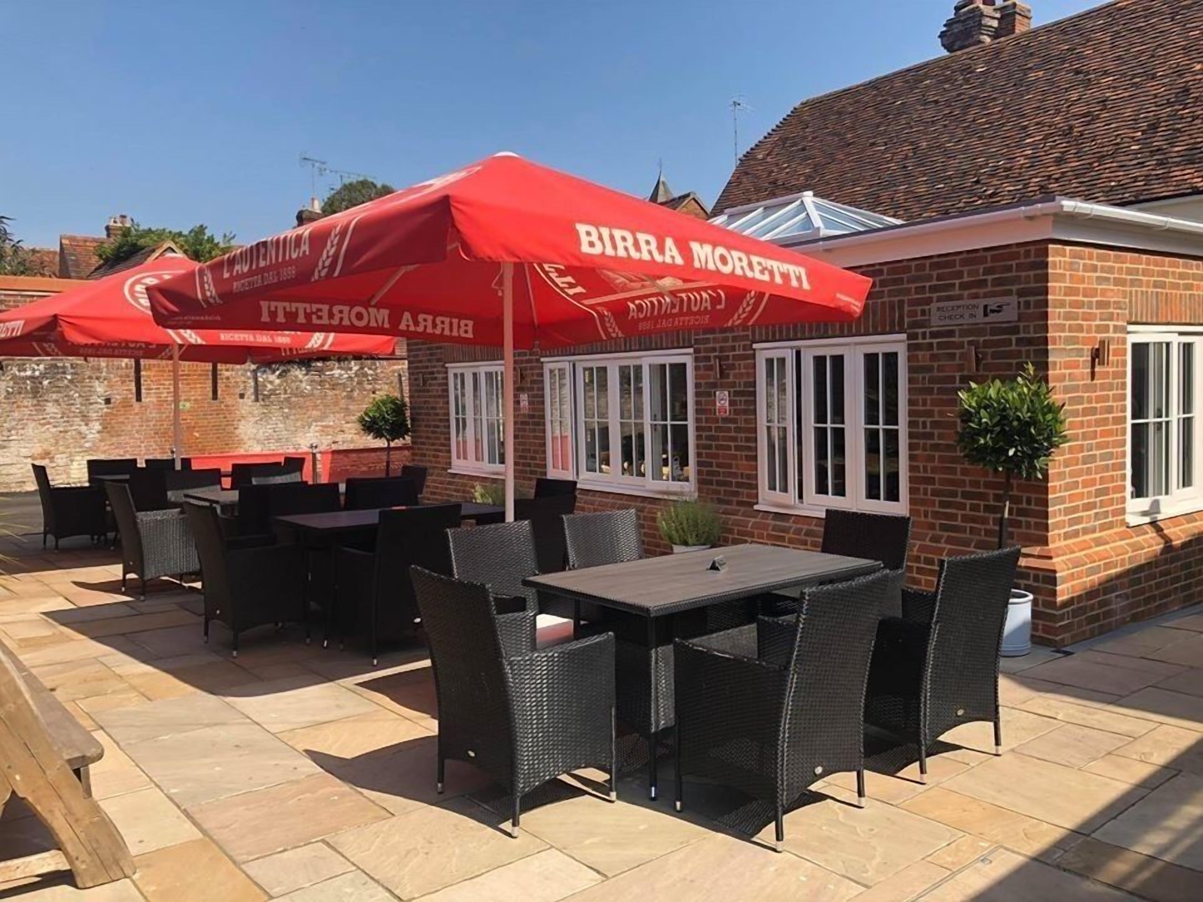 An outdoor seating area with red umbrellas labeled "Birra Moretti," featuring wicker tables and chairs.