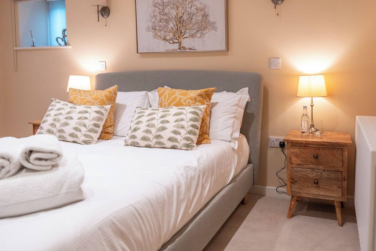A neatly made bed with patterned pillows, a bedside lamp, and a small wooden nightstand.