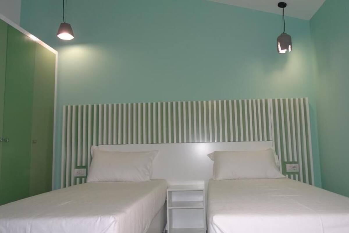 Una habitación con dos camas, un cabecero a rayas y lámparas colgantes.