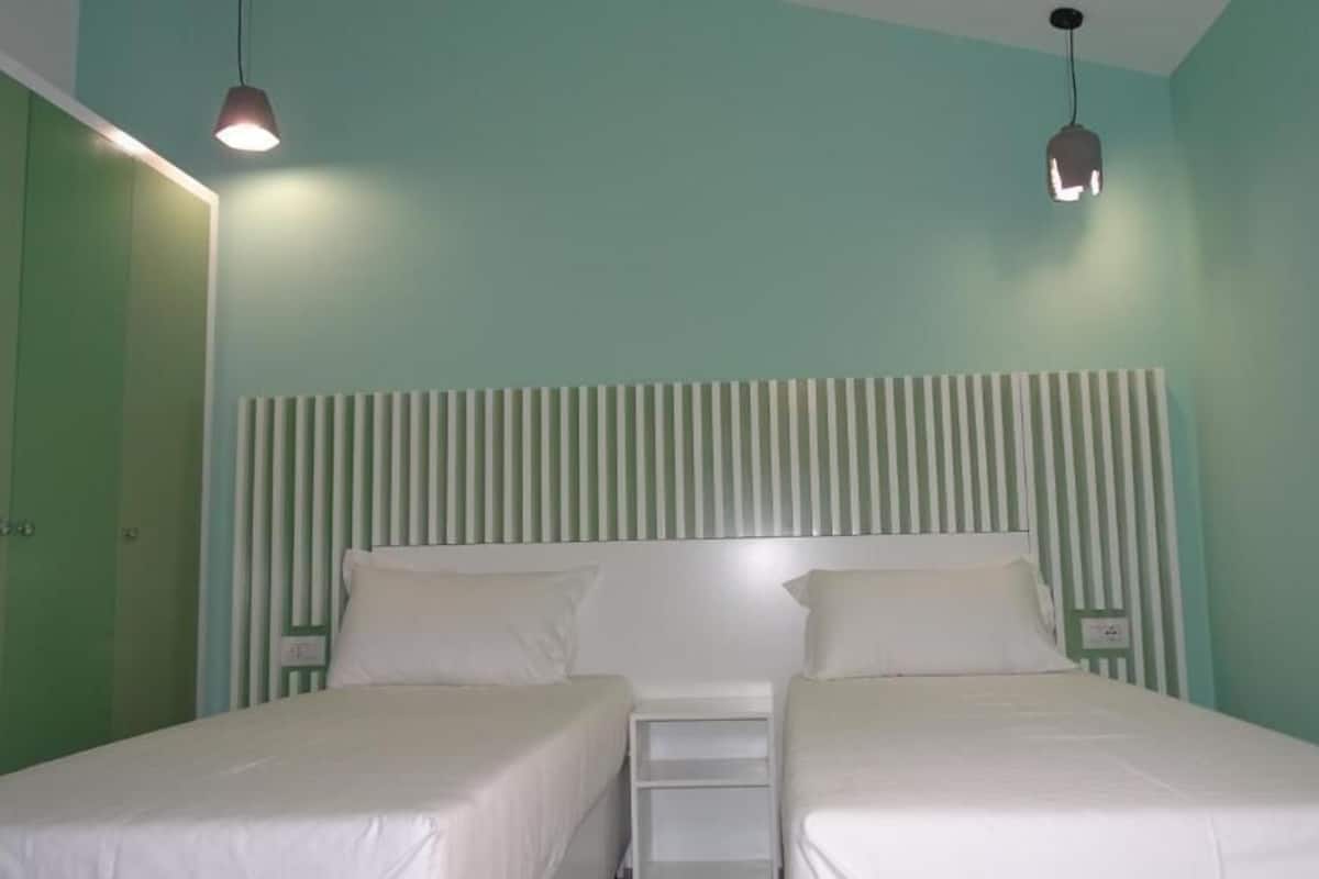 Une chambre avec deux lits, une tête de lit à rayures et des lampes suspendues.