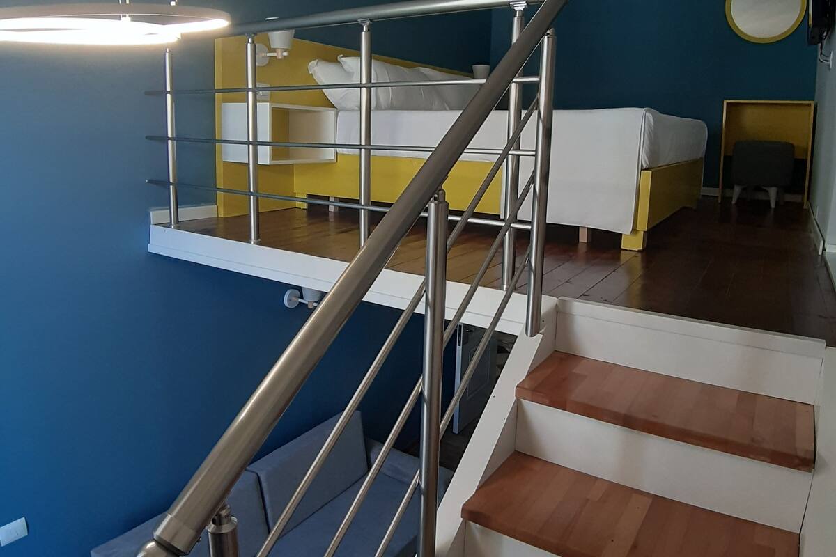 Una habitación de hotel moderna con una escalera, una cama, un escritorio y un espejo redondo.