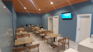Un espace repas moderne avec des tables et des chaises, un comptoir équipé d’appareils de cuisine et un téléviseur fixé au mur.