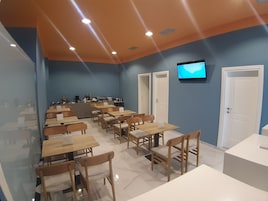 Un comedor moderno con mesas y sillas, una barra con equipo de cocina y un televisor en la pared.