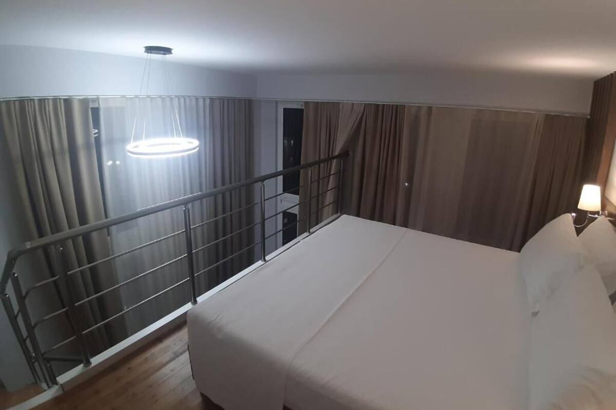 Una habitación de hotel con una cama, un balcón con barandilla y una lámpara colgante.