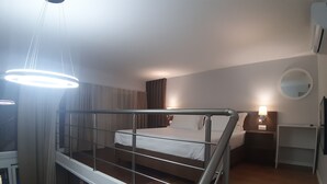 Une chambre d’hôtel avec un lit, un bureau, une chaise, un miroir et un escalier.